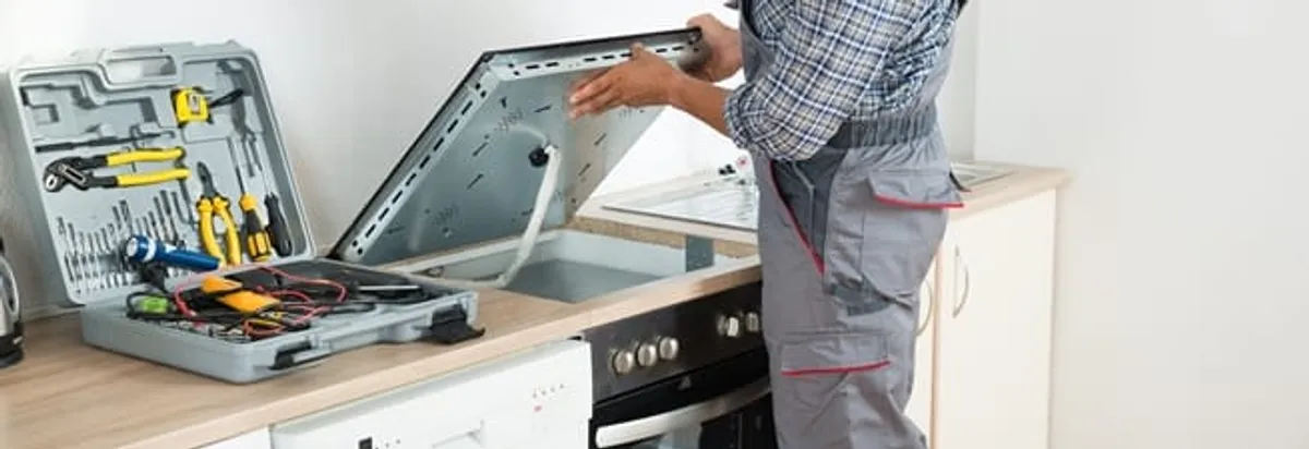Cooktop repair technician lifting a built-in stovetop for service in Indianapolis, IN